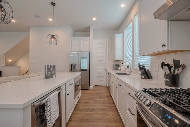 kitchen featuring stainless steel appliances, exhaust hood, sink, white cabinets, and beverage cooler