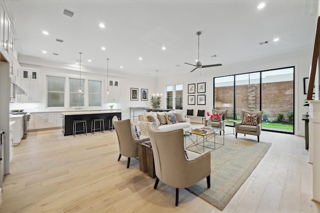 living room featuring a wealth of natural light, ceiling fan with notable chandelier, light wood-type flooring, and ornamental molding