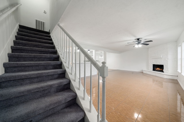 stairs featuring tile patterned floors, ceiling fan, and a fireplace