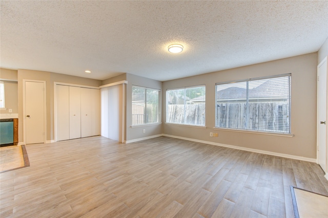 unfurnished living room with light wood-type flooring and a textured ceiling