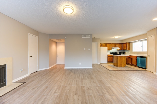 kitchen with a textured ceiling, sink, stainless steel dishwasher, white fridge, and light wood-type flooring