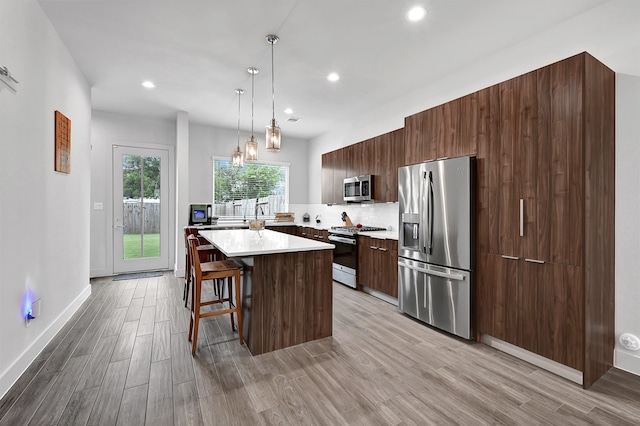 kitchen featuring a kitchen breakfast bar, light hardwood / wood-style flooring, appliances with stainless steel finishes, decorative light fixtures, and a kitchen island