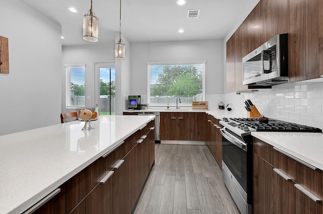 kitchen featuring light stone countertops, hanging light fixtures, stainless steel appliances, light hardwood / wood-style floors, and decorative backsplash