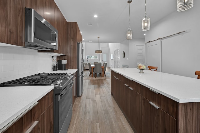 kitchen with stainless steel appliances, a barn door, light hardwood / wood-style flooring, decorative light fixtures, and decorative backsplash