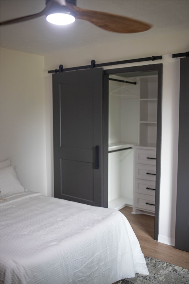 bedroom featuring a closet, a barn door, ceiling fan, and wood-type flooring