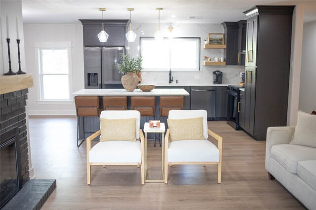 kitchen featuring stainless steel appliances, tasteful backsplash, hanging light fixtures, a fireplace, and light hardwood / wood-style flooring