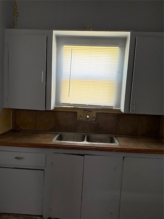 kitchen featuring white cabinetry, a sink, tile countertops, and decorative backsplash