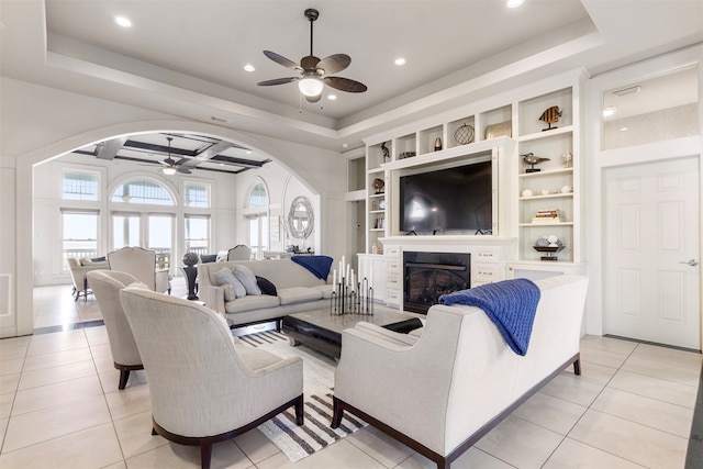 tiled living room with ceiling fan, a raised ceiling, and built in shelves