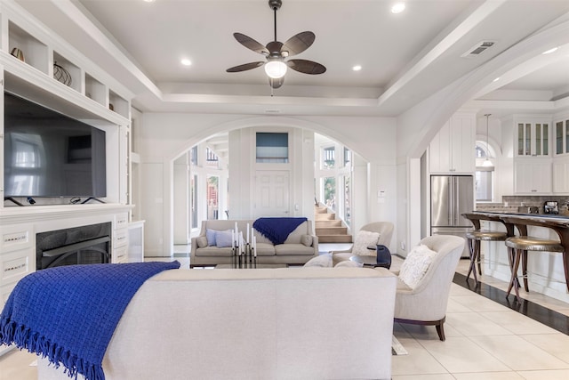 tiled living room with ceiling fan and a raised ceiling