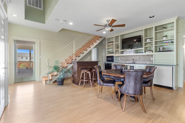 dining space featuring light wood-type flooring, ceiling fan, and indoor wet bar