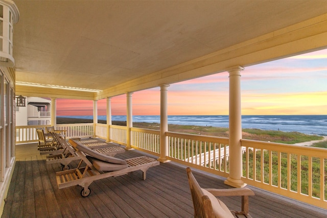 deck at dusk with a water view and a view of the beach