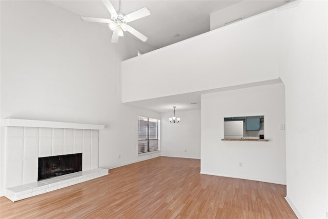 unfurnished living room featuring light hardwood / wood-style flooring, a tiled fireplace, ceiling fan with notable chandelier, and a towering ceiling