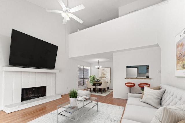 living room featuring a fireplace, hardwood / wood-style floors, ceiling fan with notable chandelier, and a towering ceiling