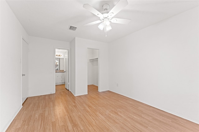 unfurnished bedroom with ensuite bath, ceiling fan, a spacious closet, light hardwood / wood-style flooring, and a closet