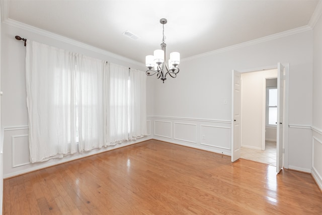 spare room featuring light wood-type flooring, a chandelier, and crown molding