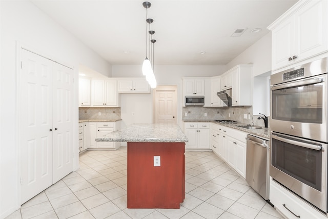 kitchen with appliances with stainless steel finishes, decorative light fixtures, light stone countertops, white cabinets, and a center island