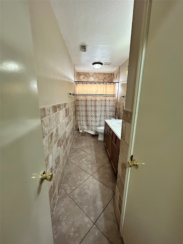 bathroom featuring vanity, a shower with curtain, tile patterned flooring, toilet, and a textured ceiling