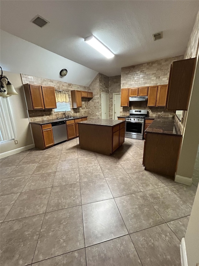 kitchen with a kitchen island, a textured ceiling, vaulted ceiling, light tile patterned floors, and appliances with stainless steel finishes