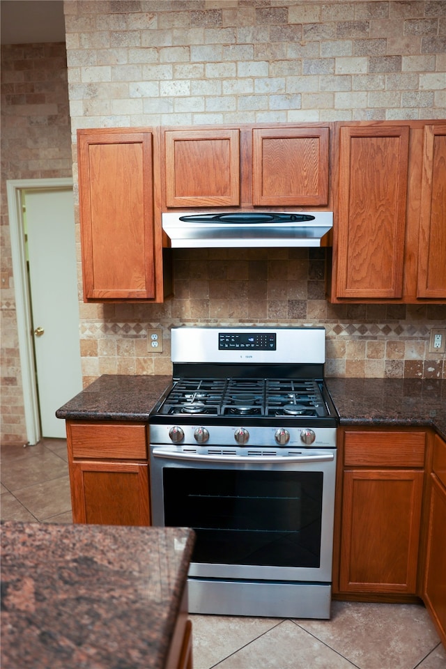 kitchen with stainless steel gas stove, backsplash, dark stone countertops, and light tile patterned flooring