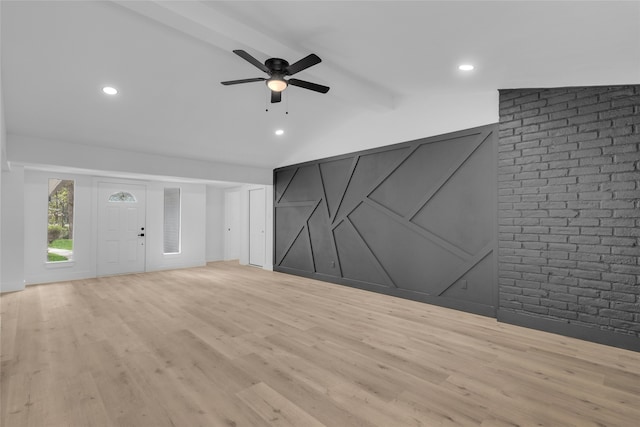 unfurnished living room featuring lofted ceiling with beams, light hardwood / wood-style floors, brick wall, and ceiling fan