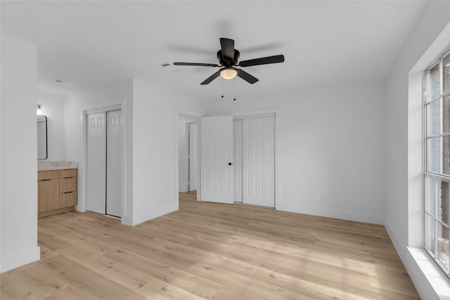 unfurnished bedroom with connected bathroom, ceiling fan, light hardwood / wood-style floors, and multiple closets