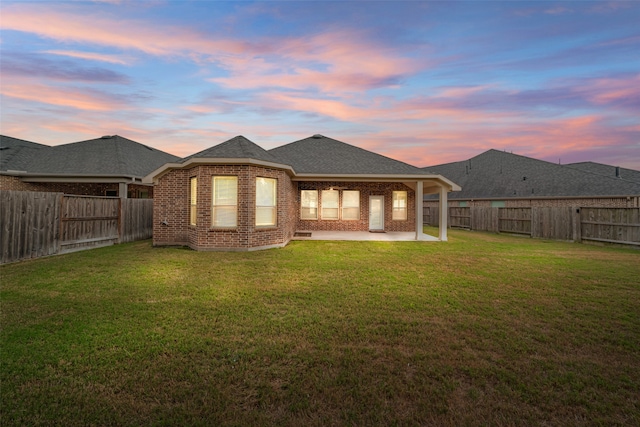 back house at dusk featuring a patio area and a lawn