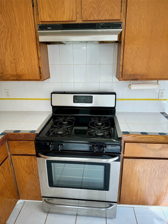 kitchen with tile countertops, decorative backsplash, gas range, and light tile patterned floors