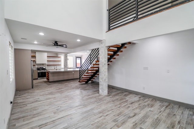 unfurnished living room with a high ceiling, light wood-type flooring, decorative columns, and ceiling fan