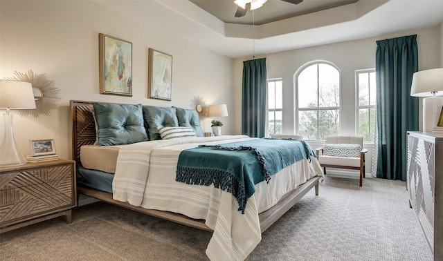 carpeted bedroom with ceiling fan and a raised ceiling