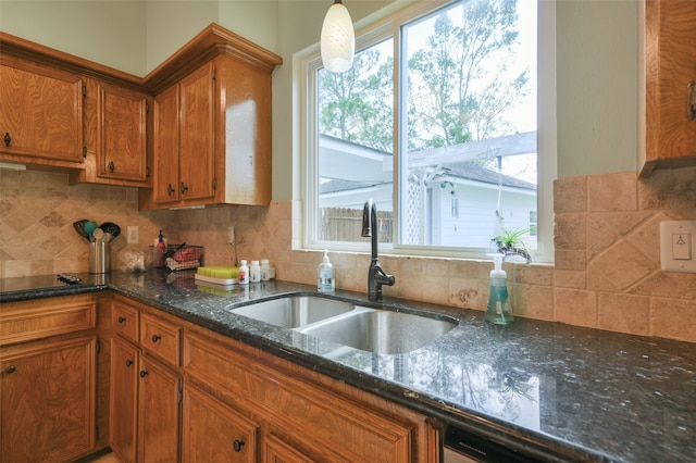 kitchen featuring backsplash, dark stone countertops, sink, and decorative light fixtures