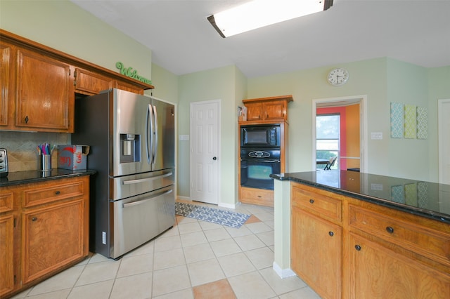 kitchen featuring decorative backsplash, light tile patterned floors, dark stone countertops, and black appliances