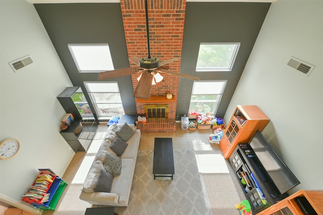 living room with ceiling fan, a towering ceiling, a fireplace, and light tile patterned floors