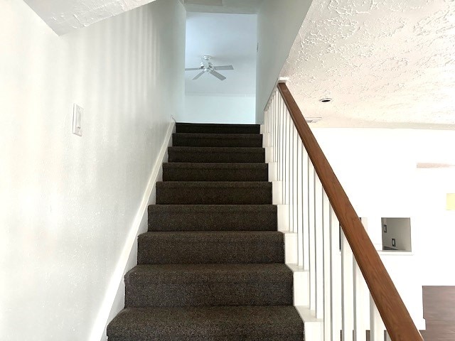 stairs featuring hardwood / wood-style floors, ceiling fan, and a textured ceiling