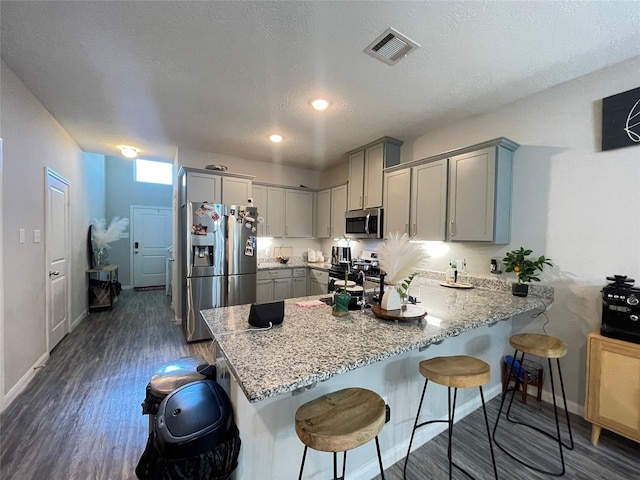 kitchen with kitchen peninsula, stainless steel appliances, gray cabinetry, and dark hardwood / wood-style flooring