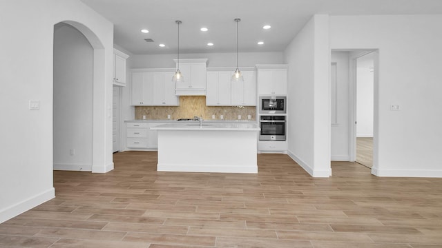 kitchen with a kitchen island with sink, stainless steel oven, decorative backsplash, and white cabinets