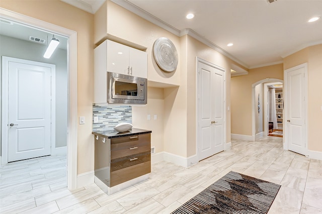 kitchen featuring white cabinets, backsplash, stainless steel microwave, and ornamental molding