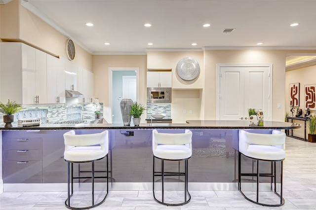 kitchen featuring white cabinets, decorative backsplash, a kitchen breakfast bar, and dark stone countertops