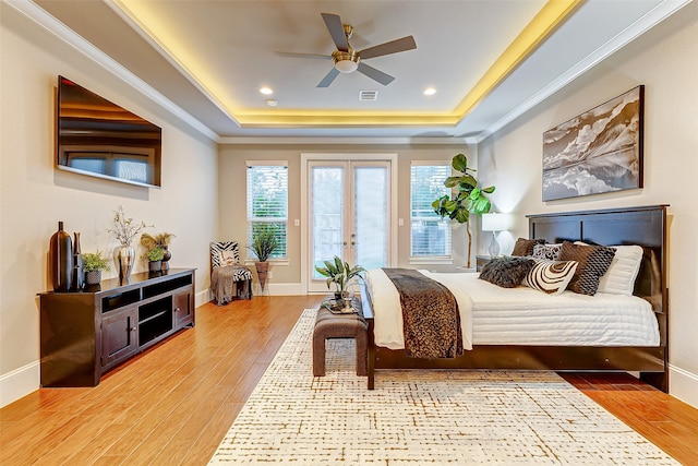 bedroom featuring french doors, access to exterior, light hardwood / wood-style floors, a tray ceiling, and ceiling fan