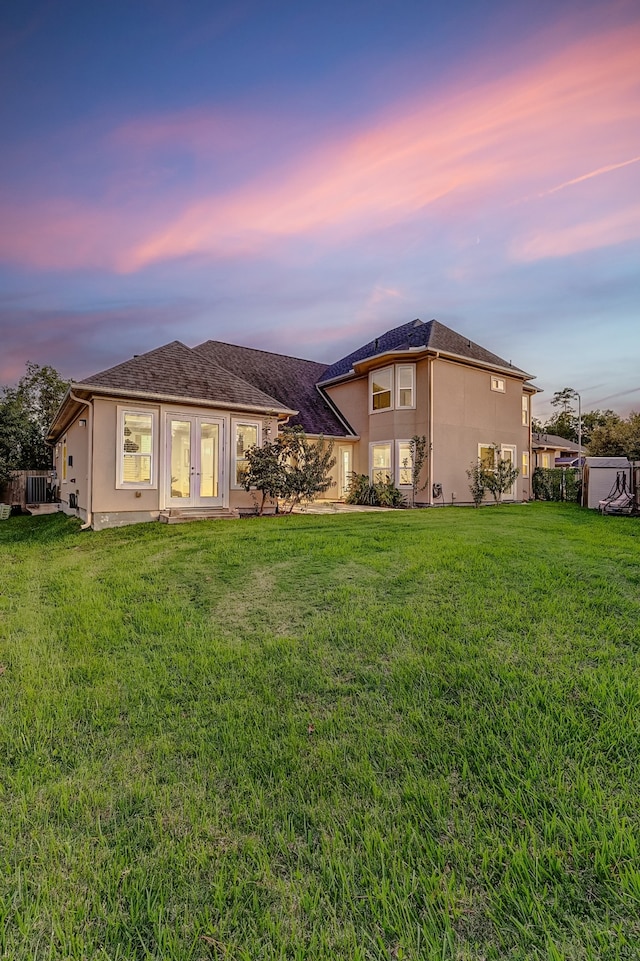 back house at dusk with a yard and french doors