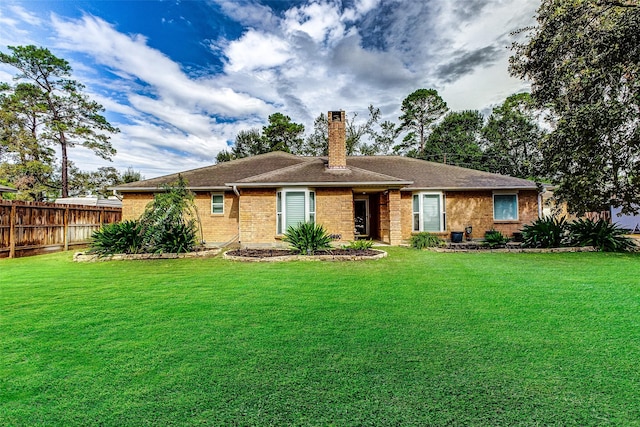 back of house featuring brick siding, fence, a chimney, and a lawn