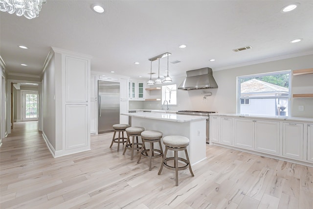 kitchen featuring a center island, wall chimney range hood, light hardwood / wood-style flooring, white cabinetry, and stainless steel appliances