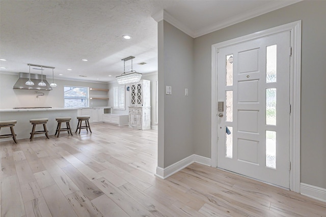 entryway featuring light wood-style floors, ornamental molding, a textured ceiling, and baseboards