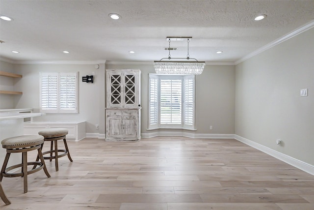 unfurnished dining area with light wood finished floors, crown molding, visible vents, and a textured ceiling