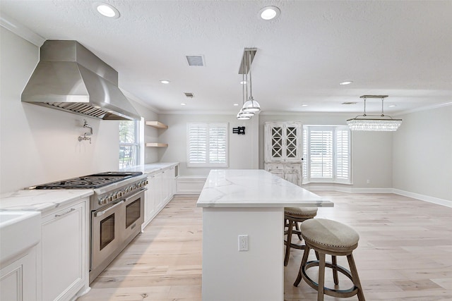 kitchen featuring range with two ovens, a center island, a kitchen bar, visible vents, and wall chimney exhaust hood