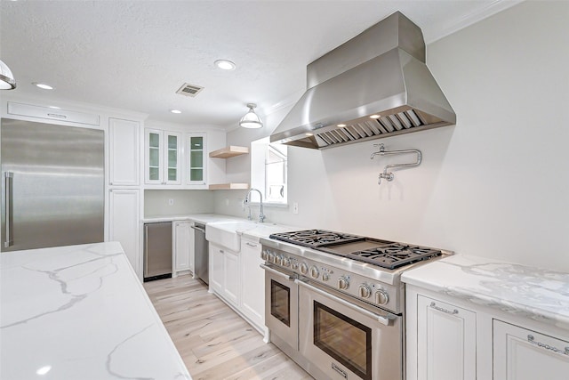 kitchen with premium appliances, wall chimney exhaust hood, glass insert cabinets, white cabinetry, and open shelves