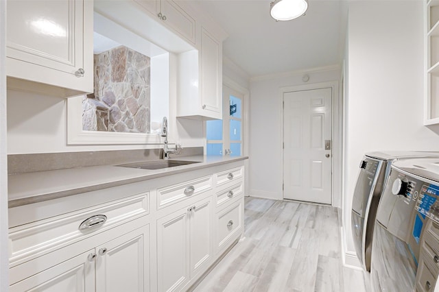 kitchen featuring crown molding, washer and clothes dryer, light countertops, white cabinets, and a sink