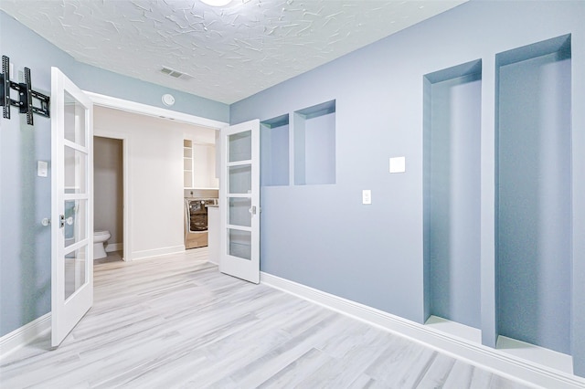 spare room with a textured ceiling, visible vents, wood finished floors, and french doors