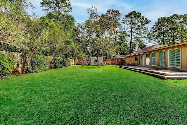 view of yard featuring a storage shed, a fenced backyard, a wooden deck, and an outbuilding