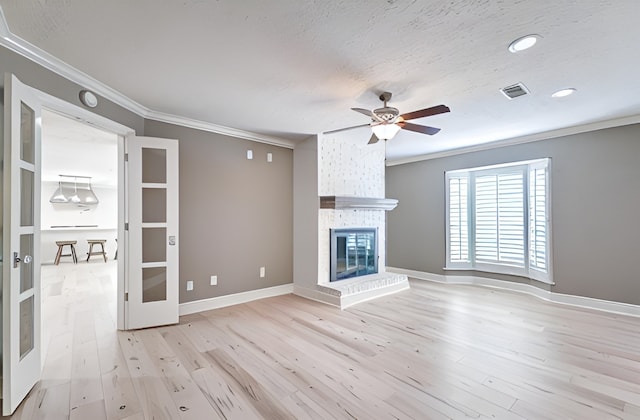 unfurnished living room featuring visible vents, crown molding, french doors, light wood-type flooring, and a fireplace