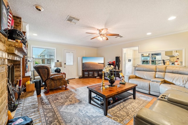 living room featuring a textured ceiling, light wood-type flooring, a fireplace, and ceiling fan